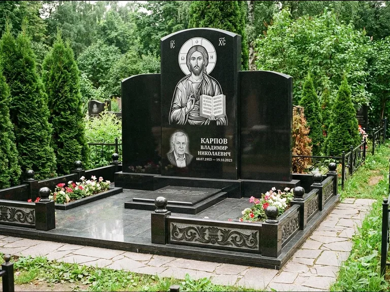 Памятник с гравировкой иконы: широкая панорамная стела с золочёным нимбом — гравировка образа Матроны Московской, цветник с белыми хризантемами, работа «Мельникова» в Ставрополе